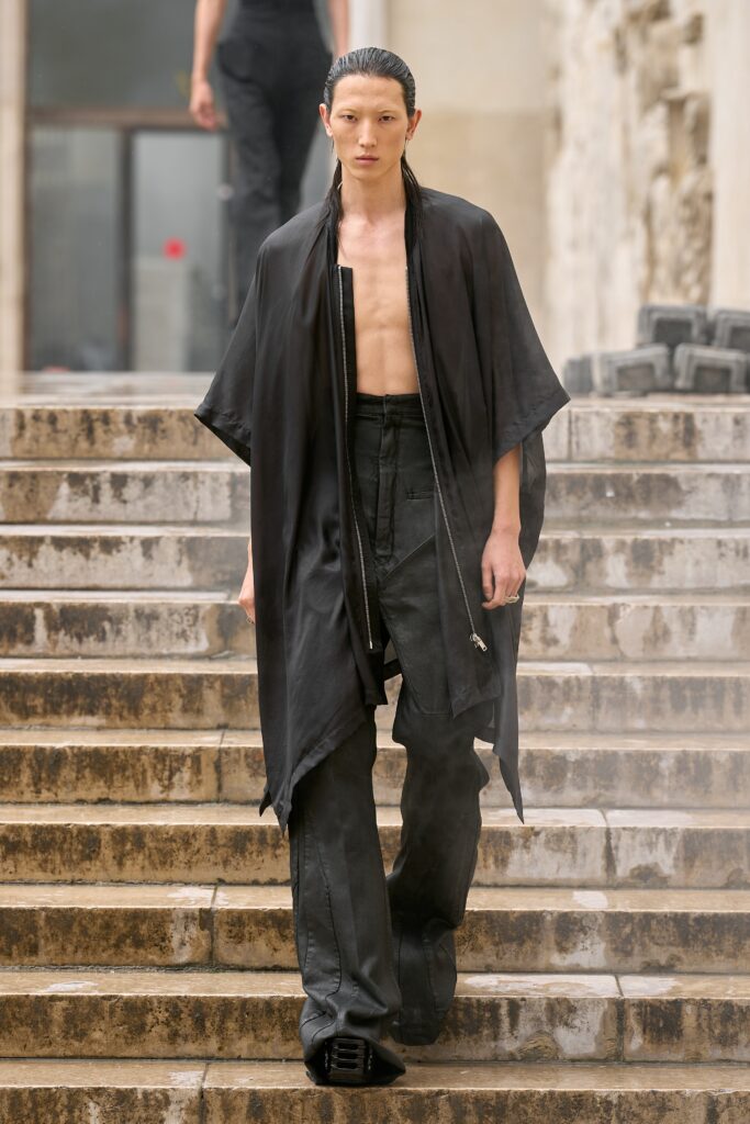 A relaxed black silk cape paired with high-waisted pants featuring an asymmetric design.