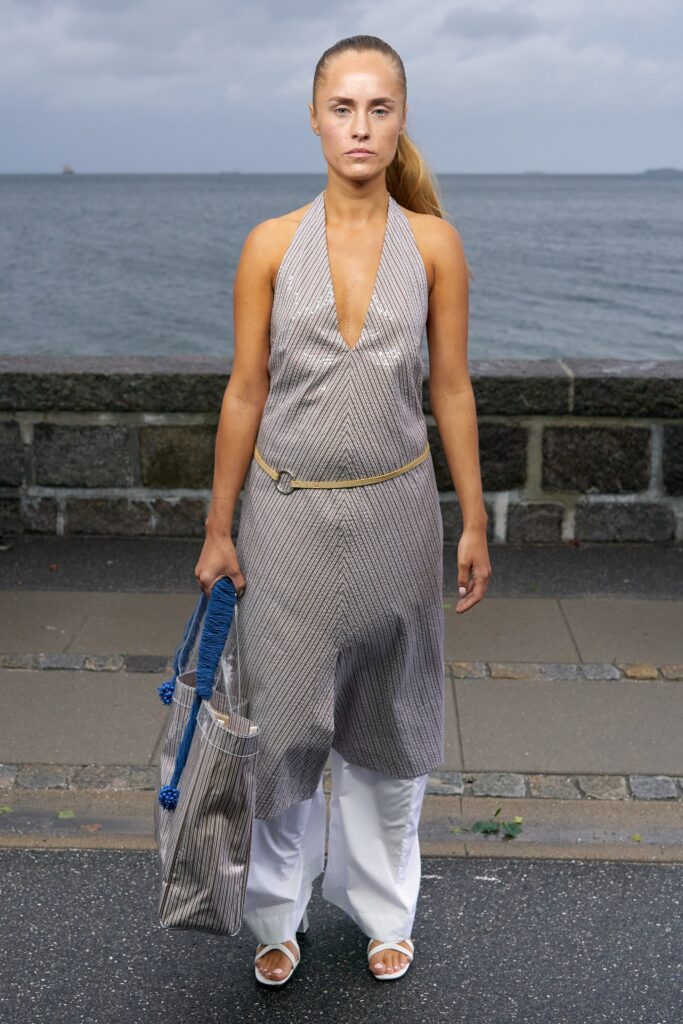A relaxed gray sleeveless dress with a V-neckline and asymmetric design paired with white pants.