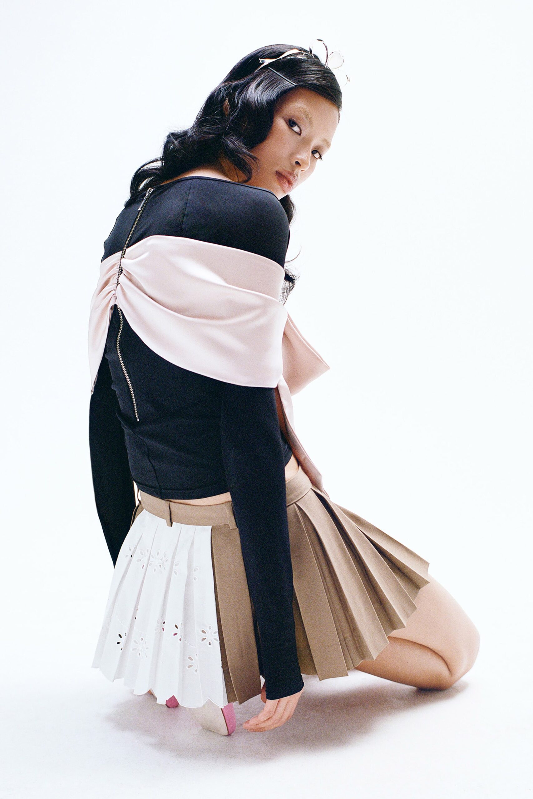 A fitted black long-sleeve top paired with a pleated beige and white skirt.