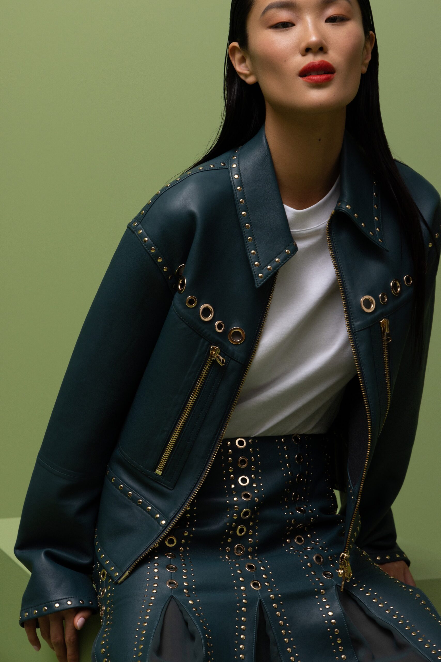 A fitted blue leather jacket with a collared neckline paired with a matching skirt featuring zippered details.