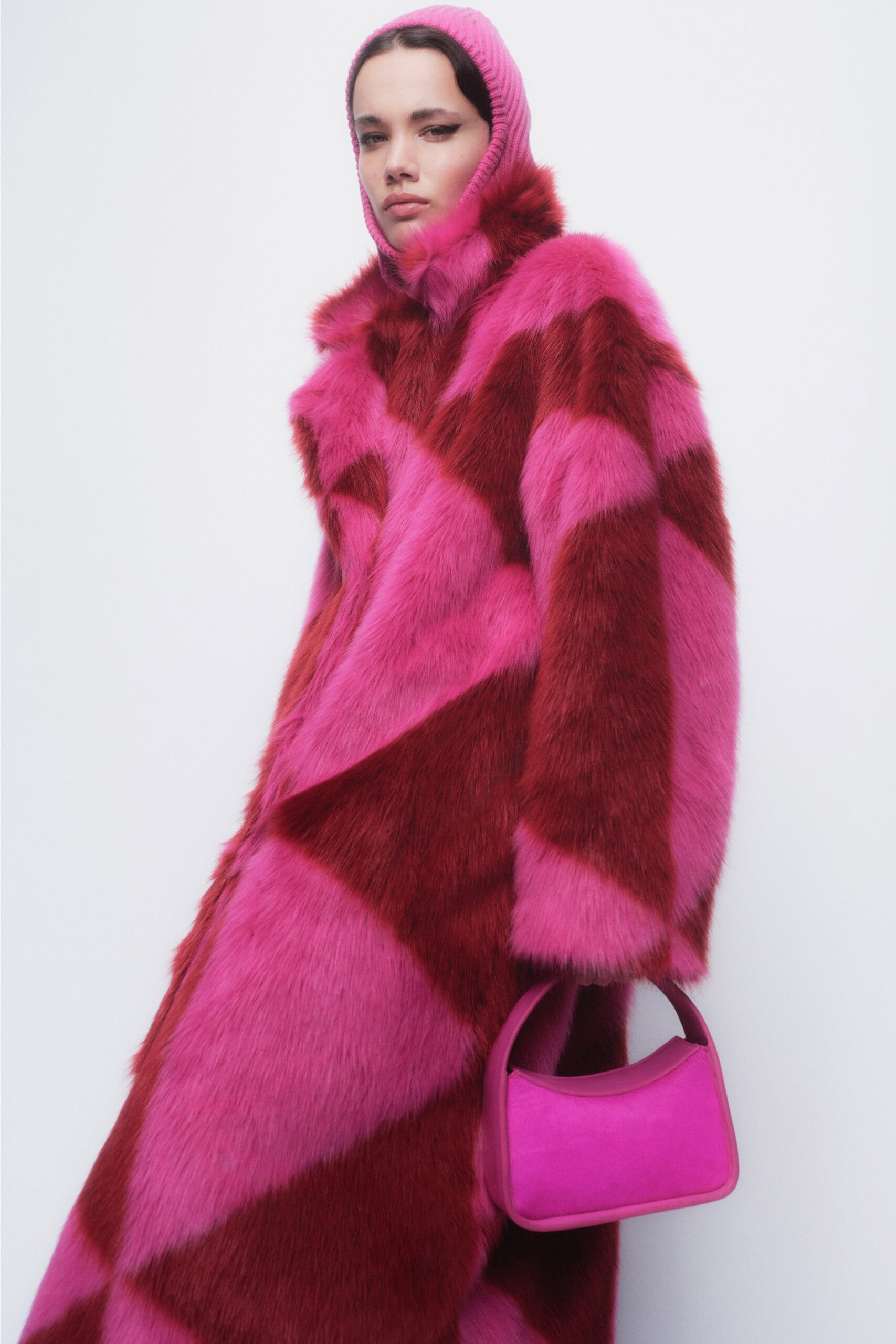 An oversized pink and red fur coat with long sleeves and a collared design featuring color-blocked patterns.