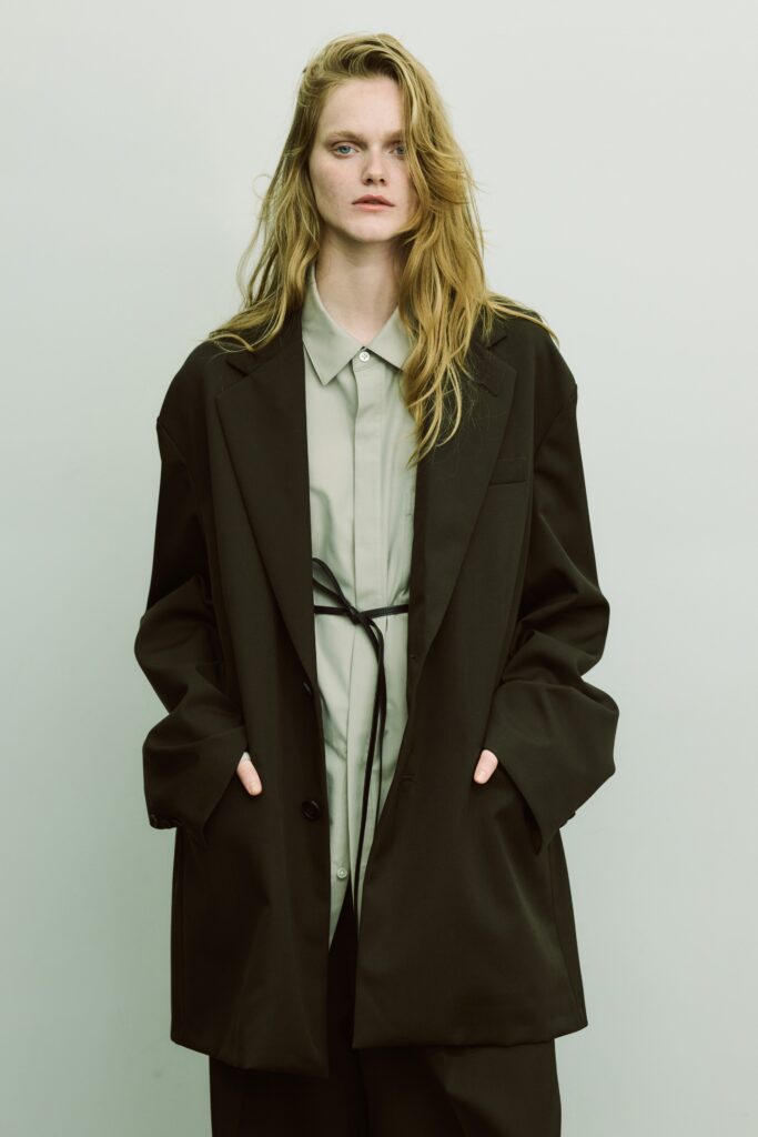 An oversized black jacket layered over a buttoned gray shirt, creating a stylish and modern look.