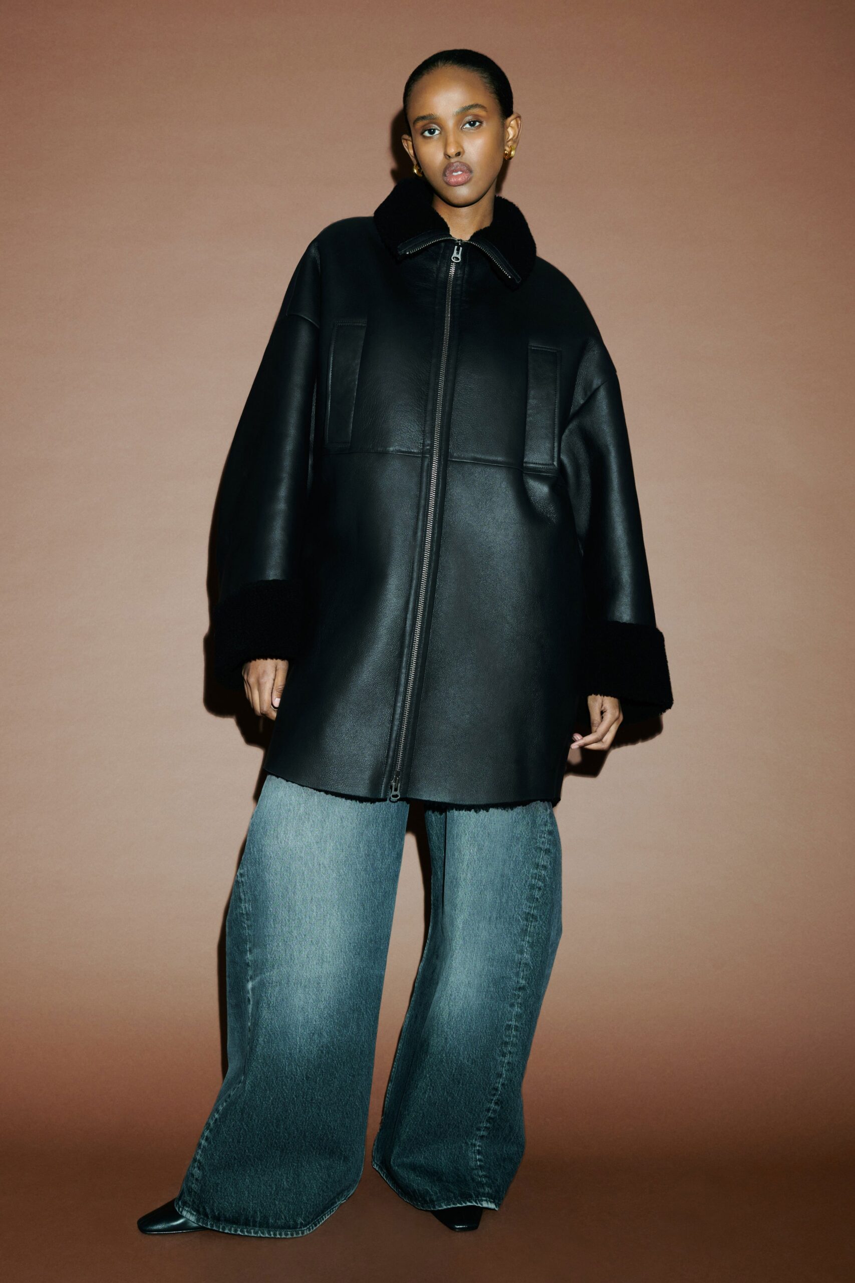 A relaxed black leather jacket with a collared neckline paired with wide-leg blue denim pants.
