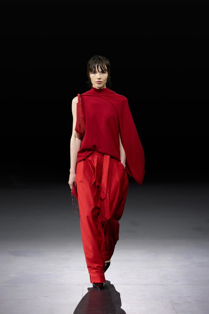 A striking red asymmetric top paired with loose-fitting red pants for a bold runway look.