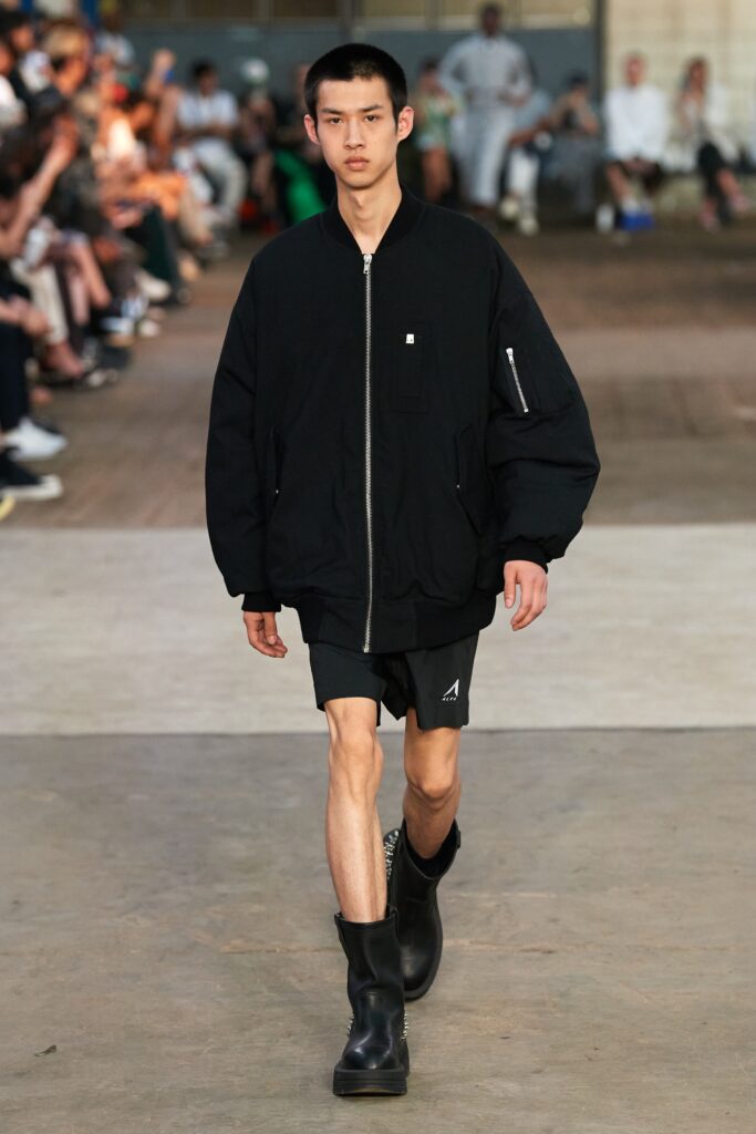 An oversized black jacket with long sleeves paired with black shorts, featuring a zippered detail.