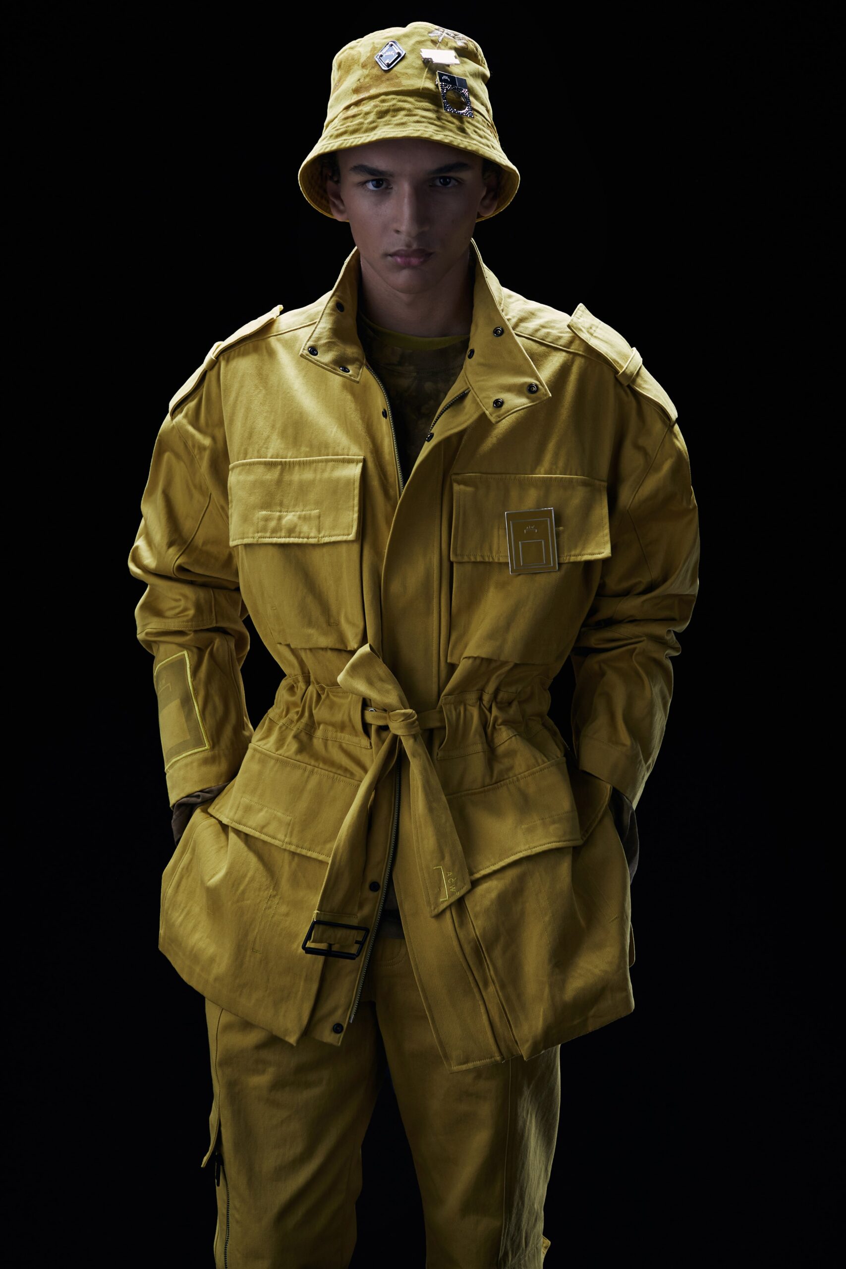This relaxed jacket in vibrant yellow features a collared design with buttoned and zippered details, creating a utilitarian aesthetic. Paired with matching pants, the ensemble exudes a cohesive look that balances functionality with bold color.