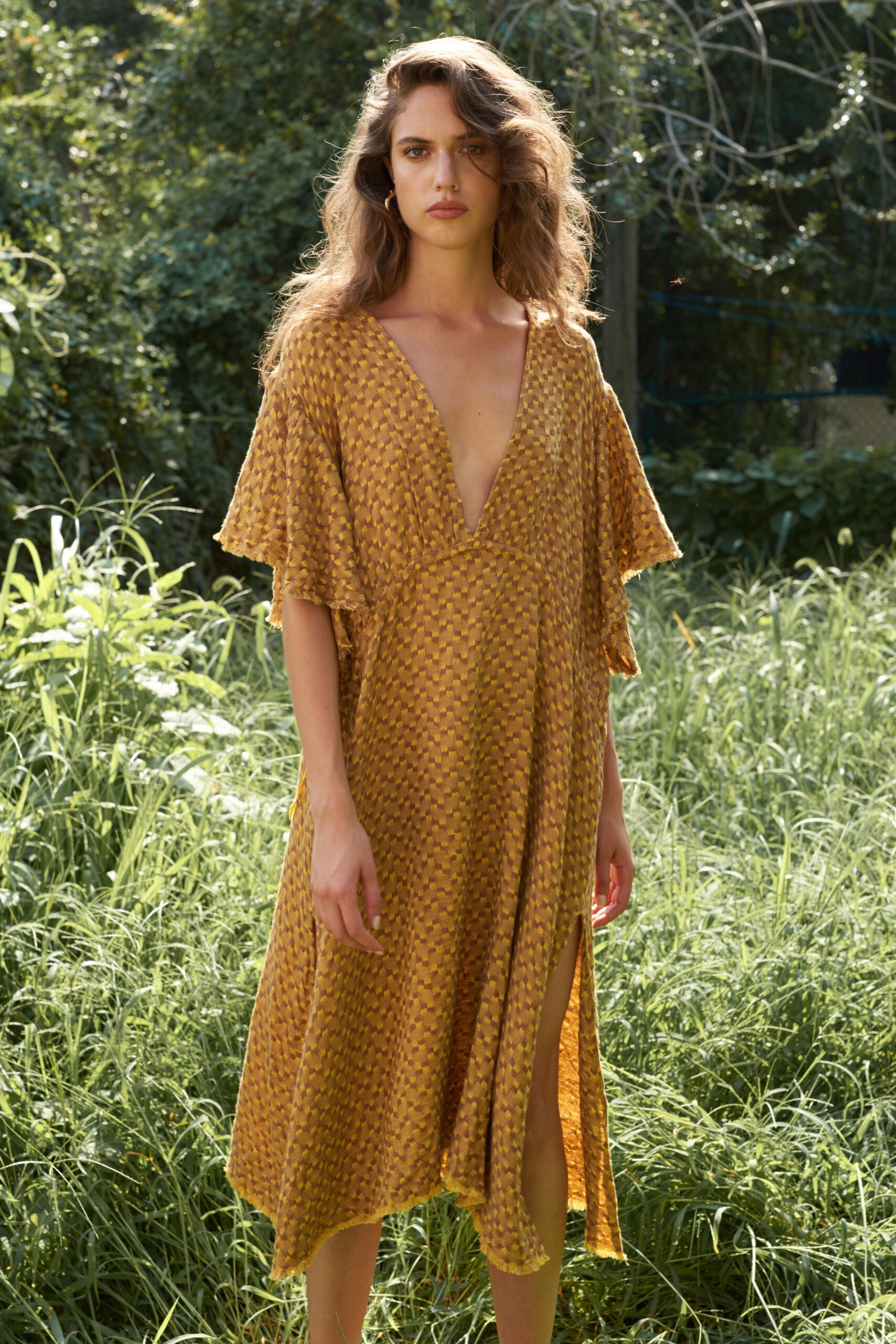A relaxed gold silk dress with short sleeves, a V-neckline, and a tiered silhouette featuring a slit.