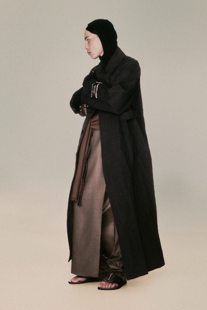 A relaxed black coat paired with brown pants, featuring a collared design and layered look.