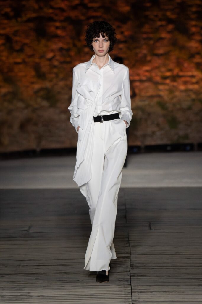 A fitted white shirt with long sleeves and asymmetric design paired with tailored pants.