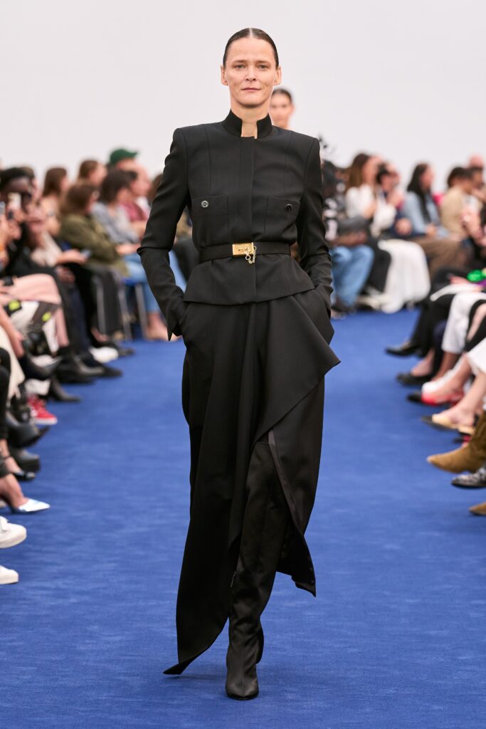 A fitted black silk dress with long sleeves, high neckline, and an asymmetric design detail.