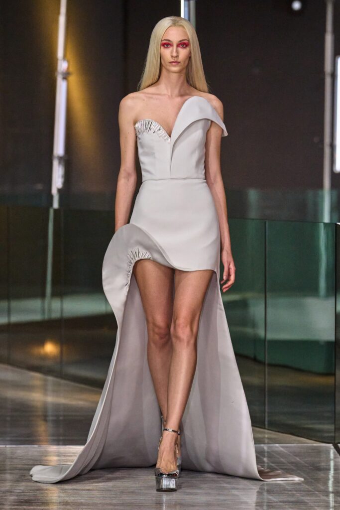 A fitted white silk dress with an off-shoulder design and asymmetric silhouette featuring a slit.