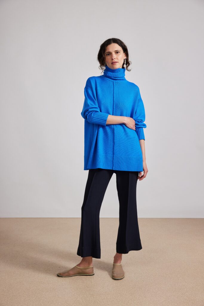 An oversized blue cotton sweater with a turtleneck paired with flared black pants.