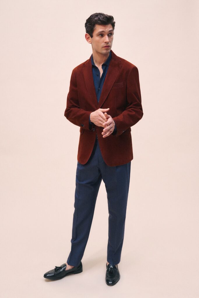 A tailored red velvet blazer paired with blue cotton pants, featuring a collared design and buttoned detail.