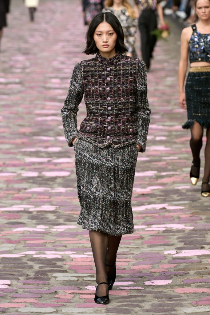A fitted black and gray tweed jacket with a collared neckline paired with a pencil skirt.