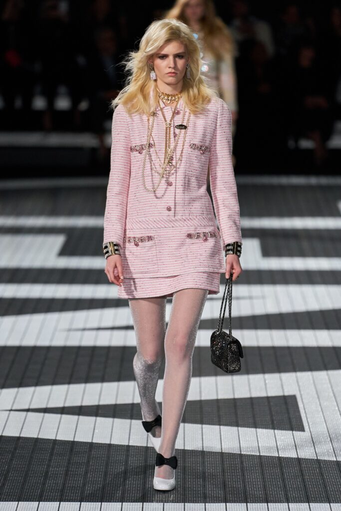 A fitted pink tweed dress with long sleeves, a collared neckline, and buttoned details.