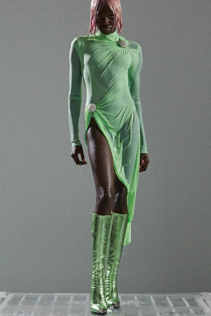 A fitted green silk dress with long sleeves, high neckline, and asymmetric draped design.