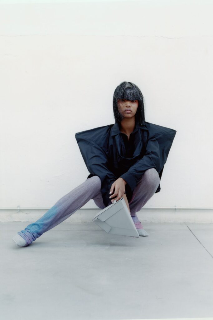 A relaxed black jacket with long sleeves and a collared design paired with gray pants featuring an asymmetric detail.
