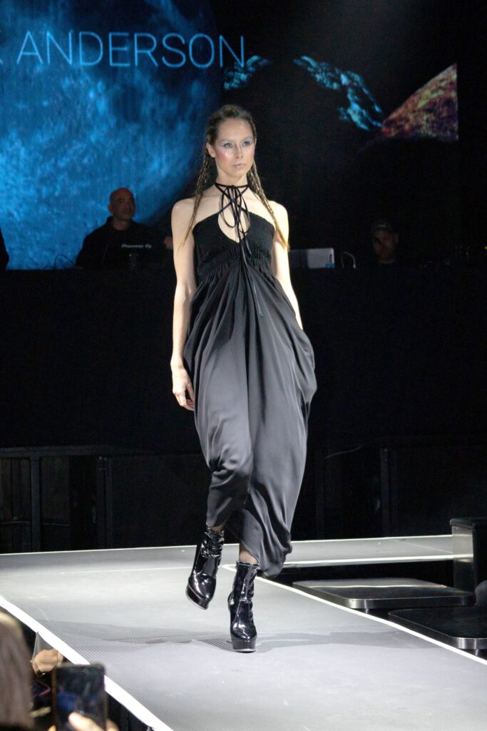 A relaxed black sleeveless dress with a high neckline and draped design.