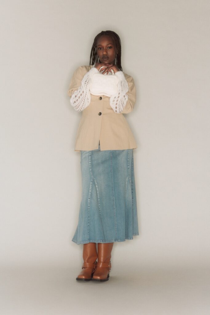 A fitted beige blazer with long sleeves and a collared neckline paired with a flared blue denim skirt.