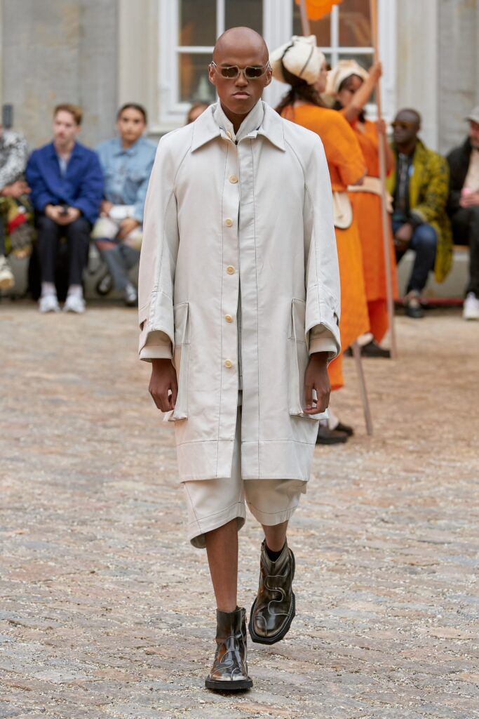 A relaxed beige cotton coat with long sleeves and a collared design, paired with shorts.