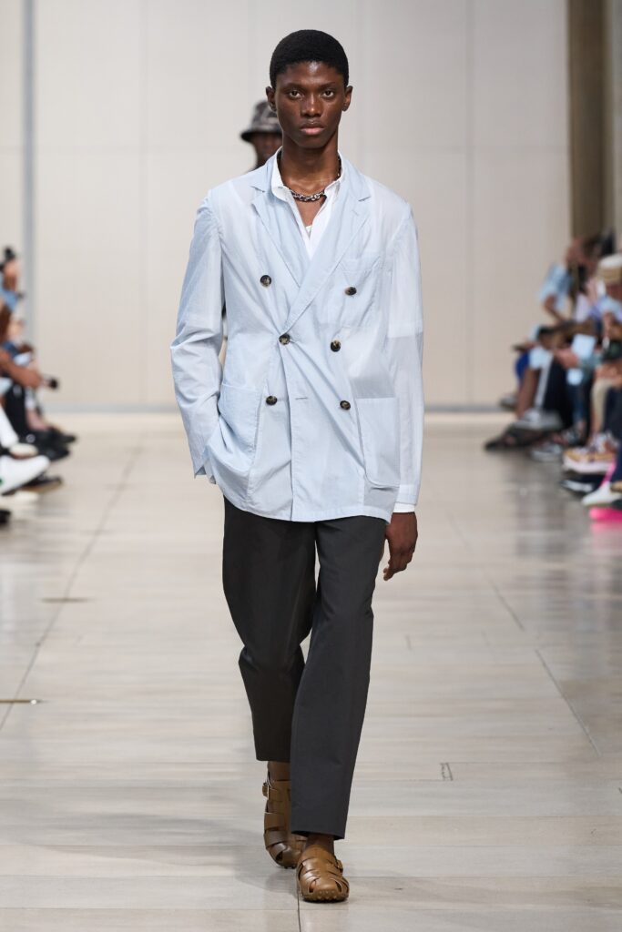 A tailored blue cotton jacket with long sleeves and collared design, paired with straight-leg gray pants.