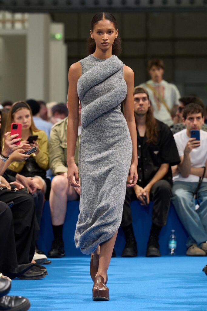 A fitted gray knit dress with a sleeveless design and draped detailing.