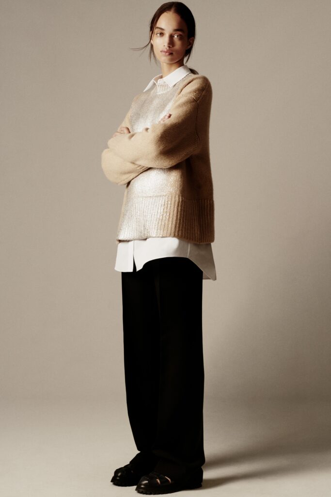 A relaxed beige sweater layered over a white collared shirt, paired with black trousers.