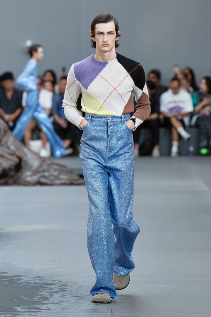 A fitted multicolor long-sleeve sweater paired with high-waisted blue wide-leg pants.