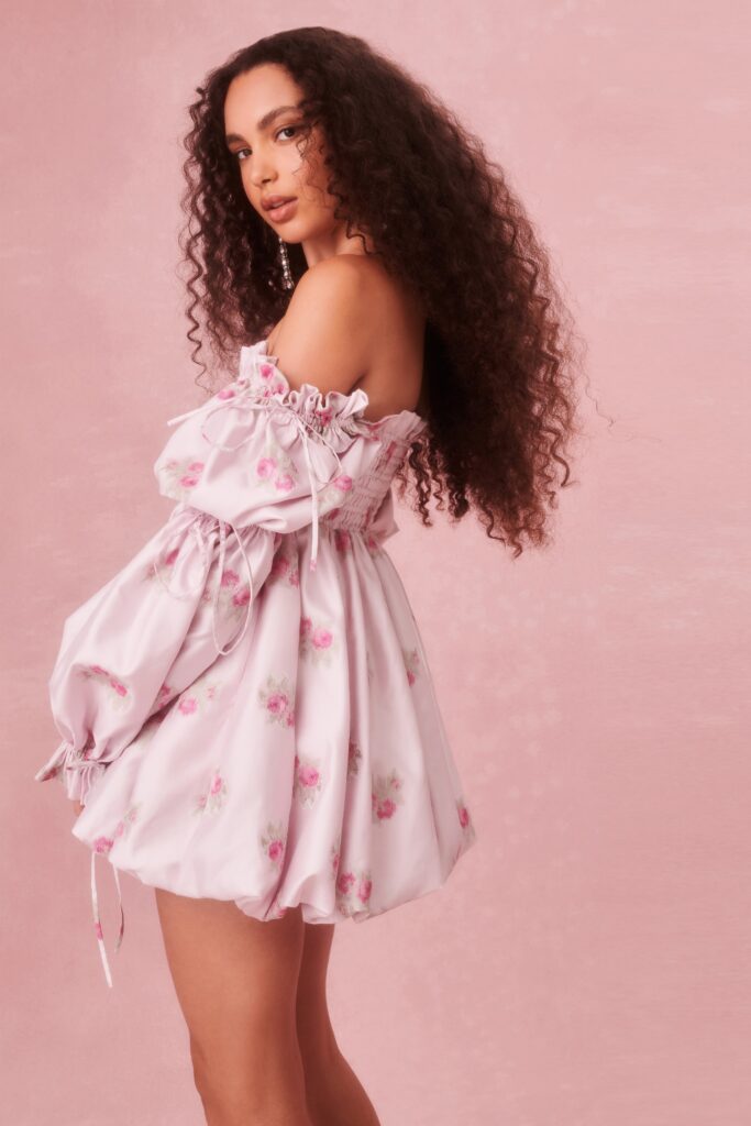 A relaxed pink silk off-shoulder dress with ruffled details and a flared silhouette.