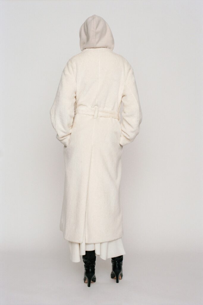 A relaxed white wool coat with long sleeves and a belted design featuring a hood.