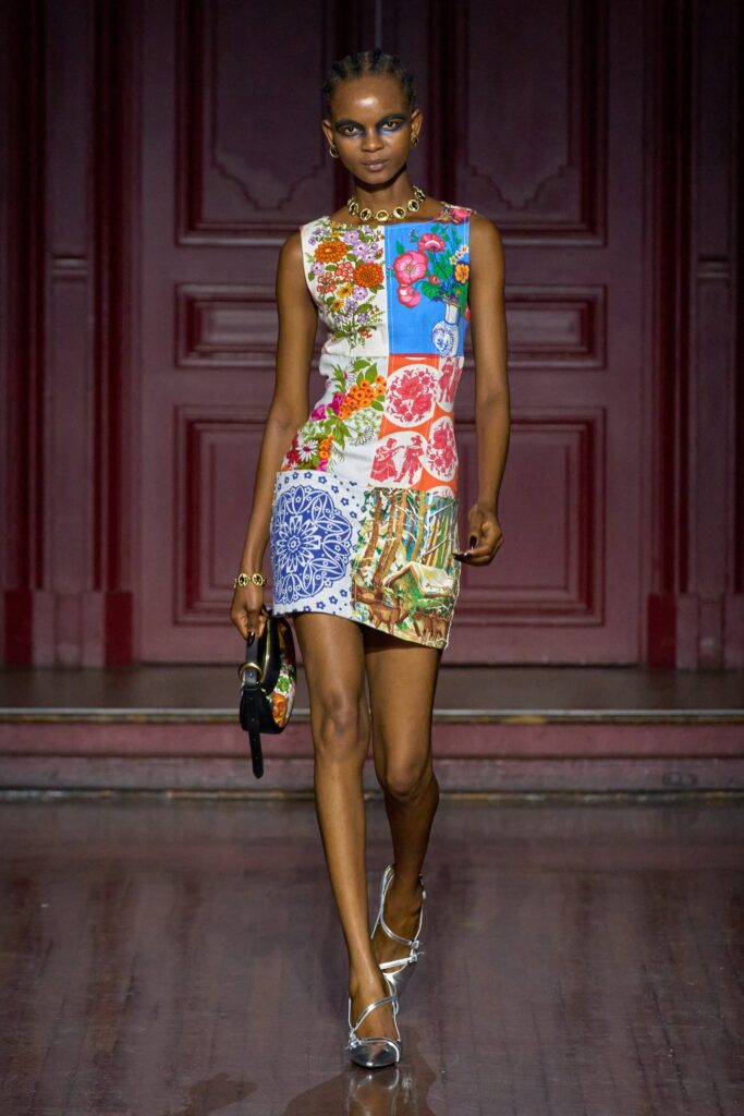 A fitted multicolor printed sleeveless dress with a high neckline and vibrant floral patterns.