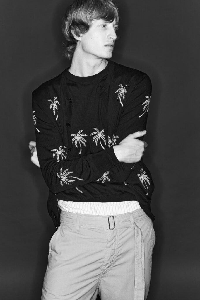 A relaxed black cardigan with embroidered palm trees, paired with beige pants.