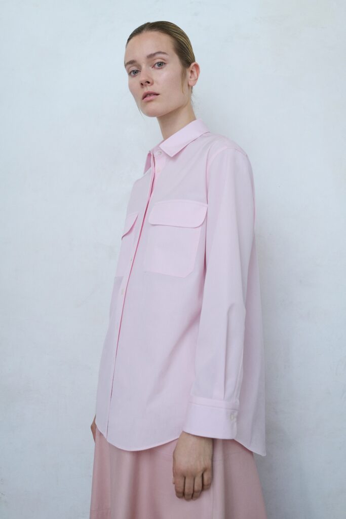 A relaxed pink cotton shirt with long sleeves and a collared neckline paired with a straight-leg skirt.
