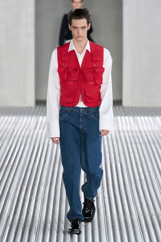 A relaxed fit red vest over a collared white shirt paired with blue denim pants.