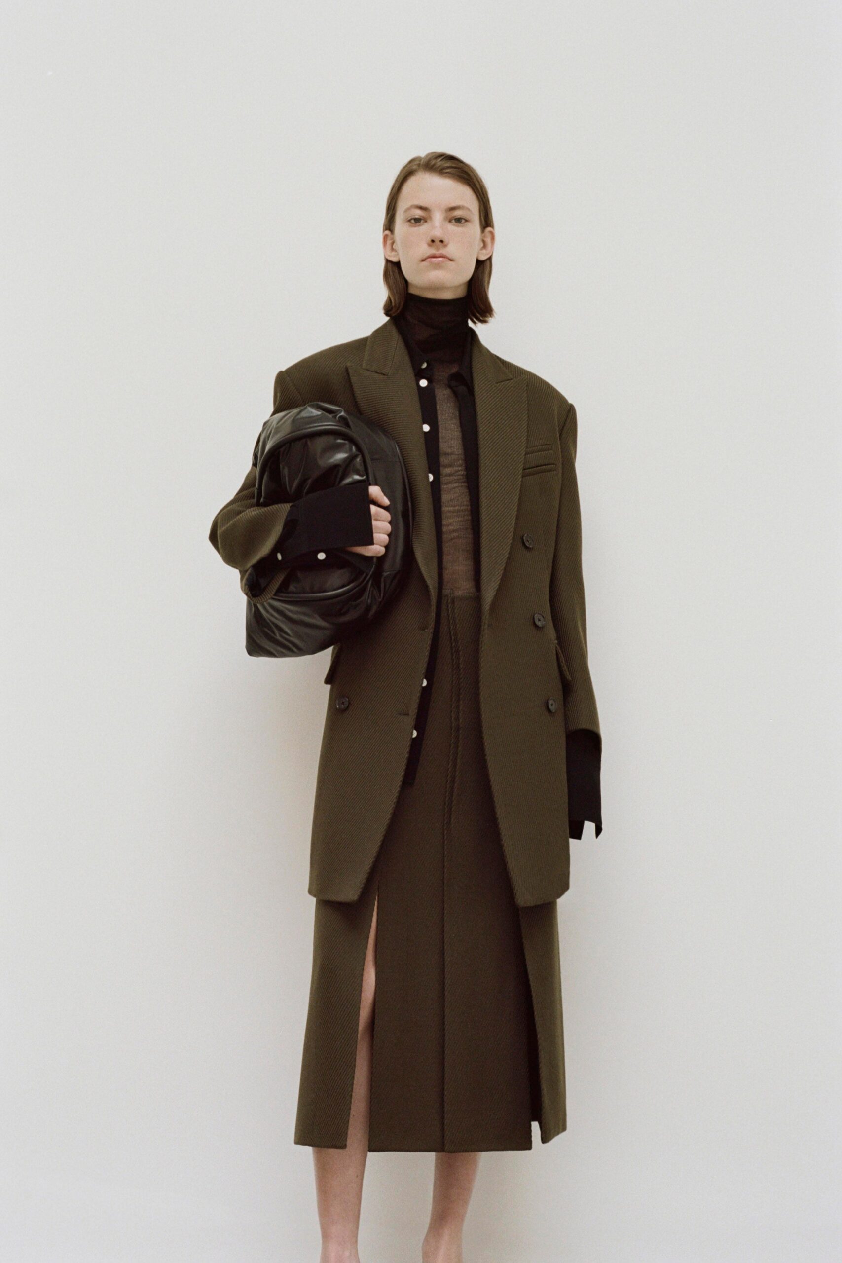 A fitted brown wool blazer with a collared neckline paired with a matching asymmetric skirt featuring a slit.