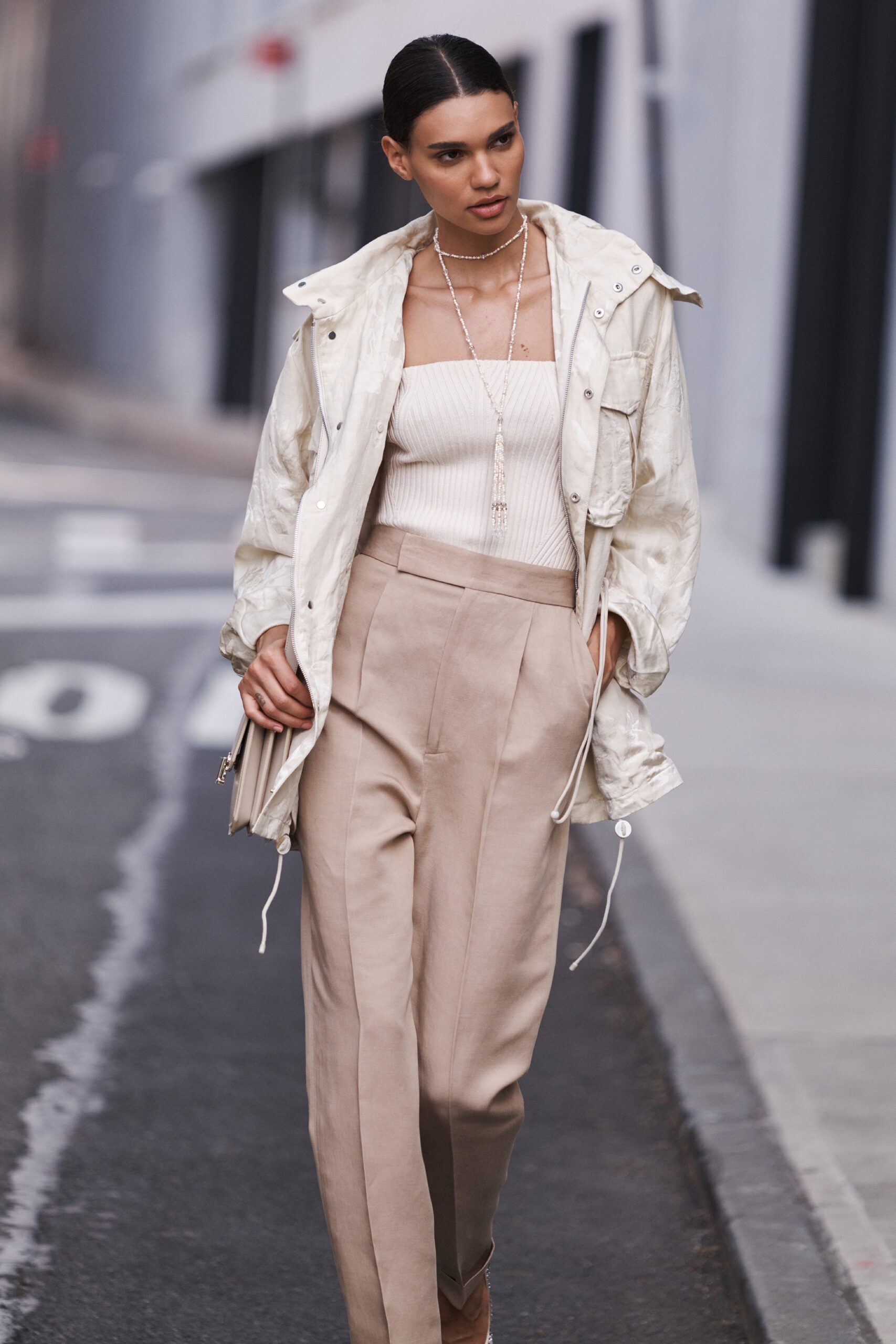 A fitted white jacket with long sleeves paired with pleated beige pants.