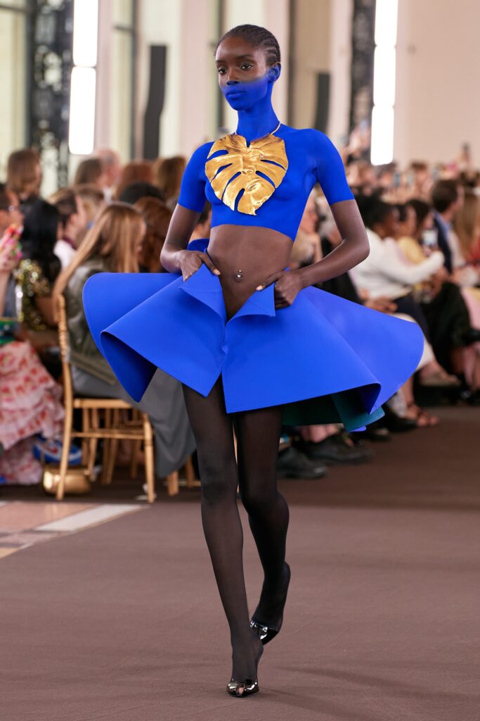 A fitted blue neoprene sleeveless dress with a high neckline and asymmetric flared silhouette.