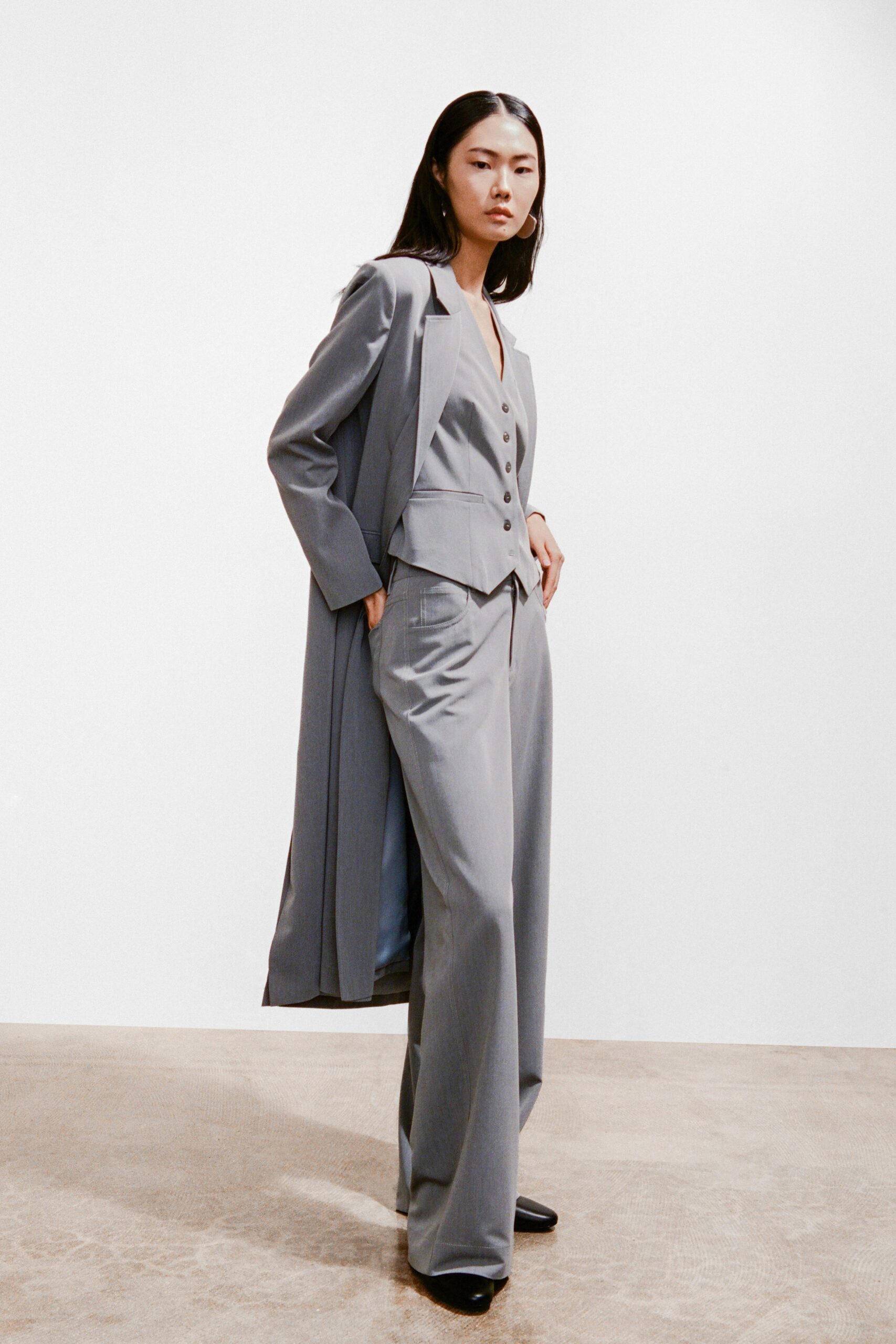 A fitted gray cotton suit featuring a collared long-sleeve jacket and wide-leg trousers.