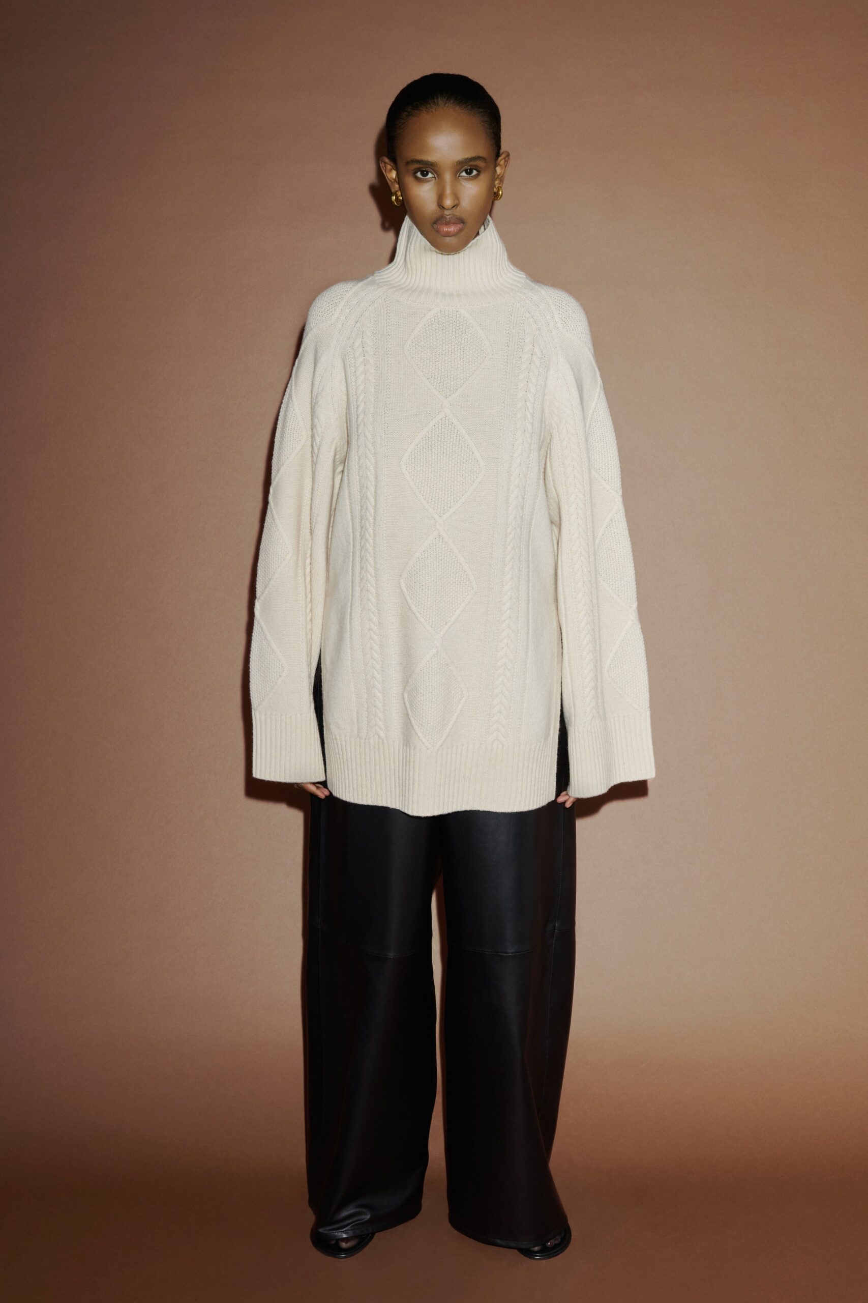 An oversized cream knit sweater with a turtleneck paired with black leather pants.