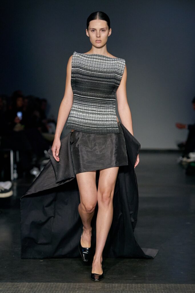 A fitted black and gray asymmetric dress with a sleeveless high-neck design.
