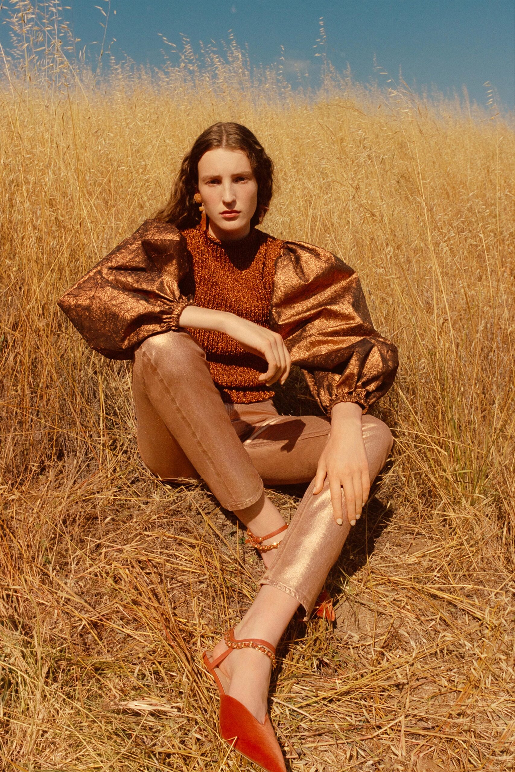 A fitted brown silk long-sleeve top paired with structured gold denim pants.