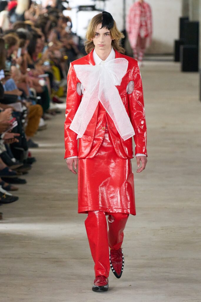 A fitted red leather suit with long sleeves, a collared design, and an asymmetric detail.