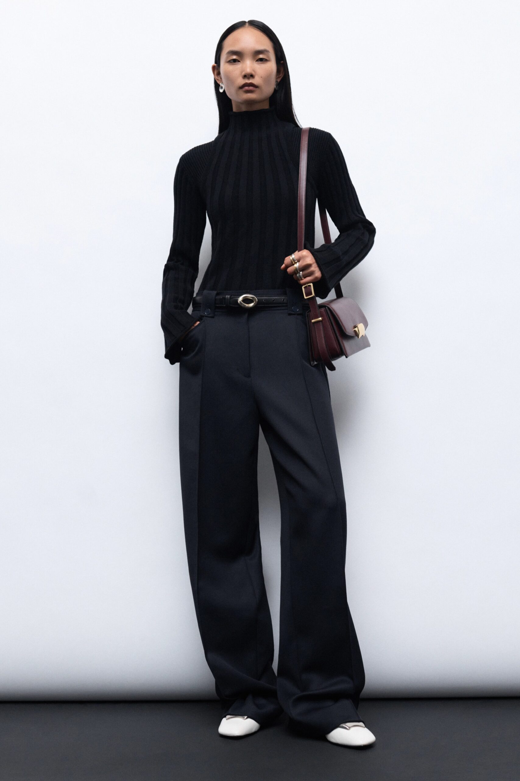 A relaxed black long-sleeve high-neck top paired with pleated wide-leg gray pants.