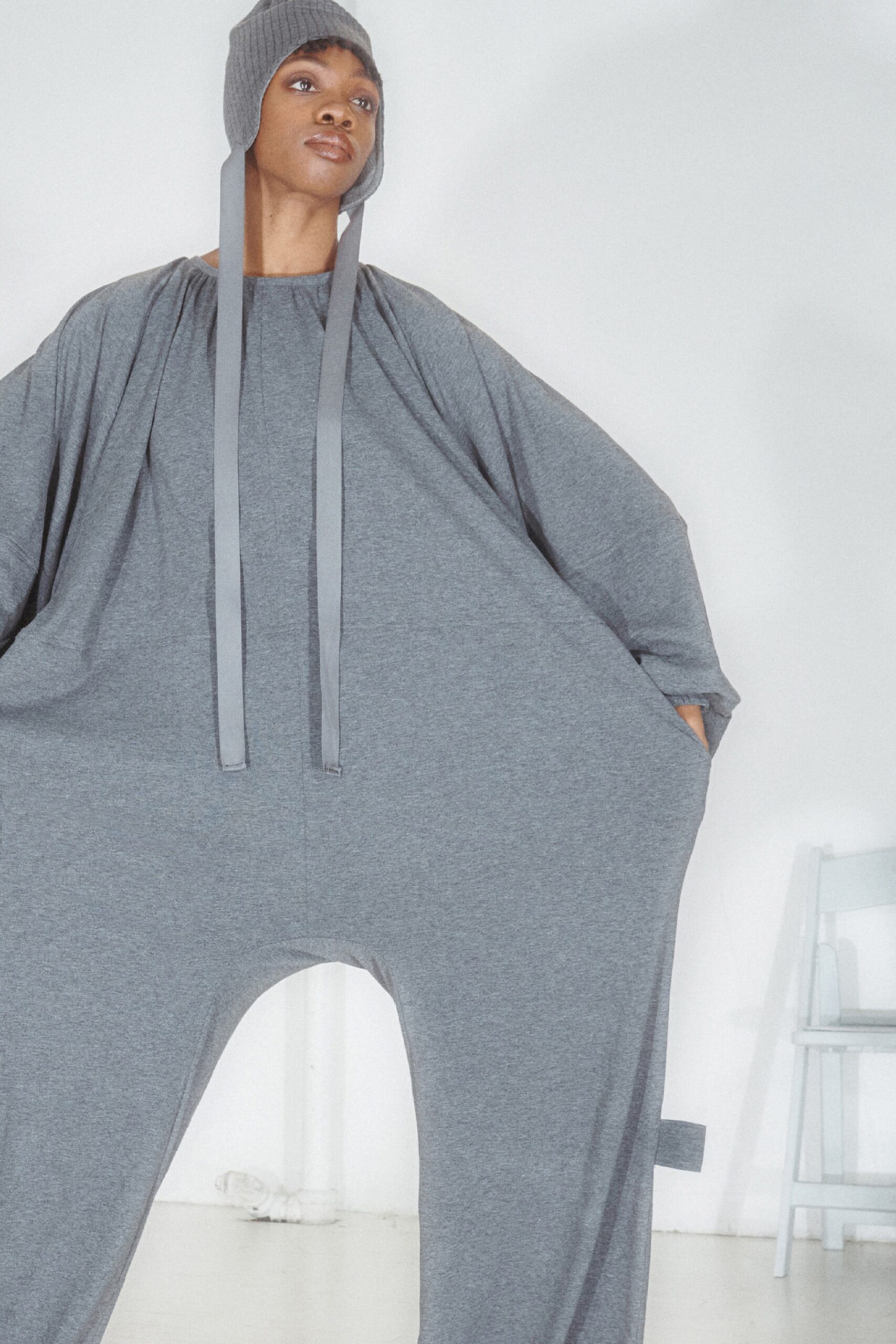 This oversized jumpsuit in soft gray cotton features a unique draped silhouette that creates a striking visual impact. The long sleeves and hood add an element of comfort, while the relaxed fit allows for effortless movement, making it an intriguing piece for modern streetwear.