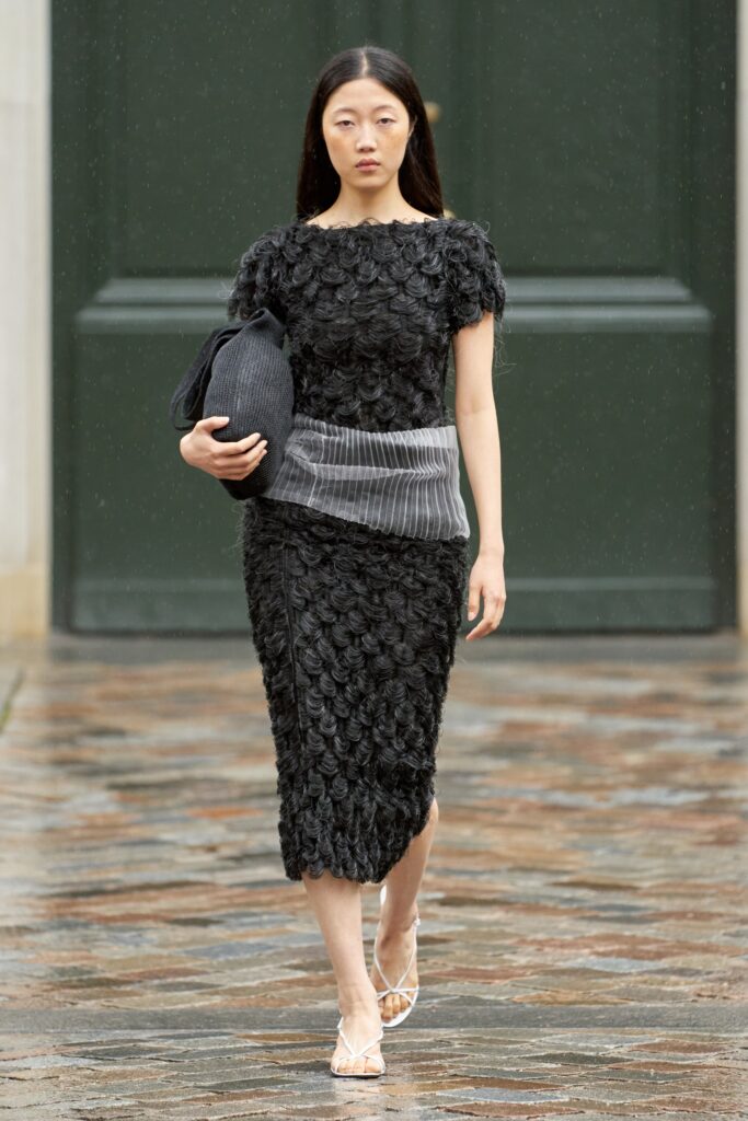 A fitted black dress with short sleeves, high neckline, and layered design details.