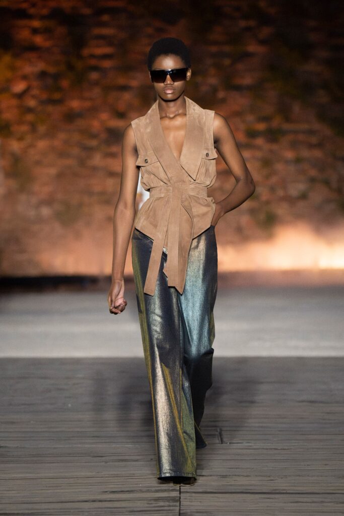 A fitted beige suede sleeveless vest paired with multicolor wide-leg pants, showcasing an asymmetric design.