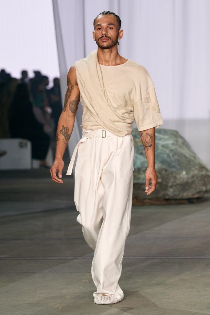 A relaxed beige cotton top with short sleeves and asymmetric design paired with white pants.