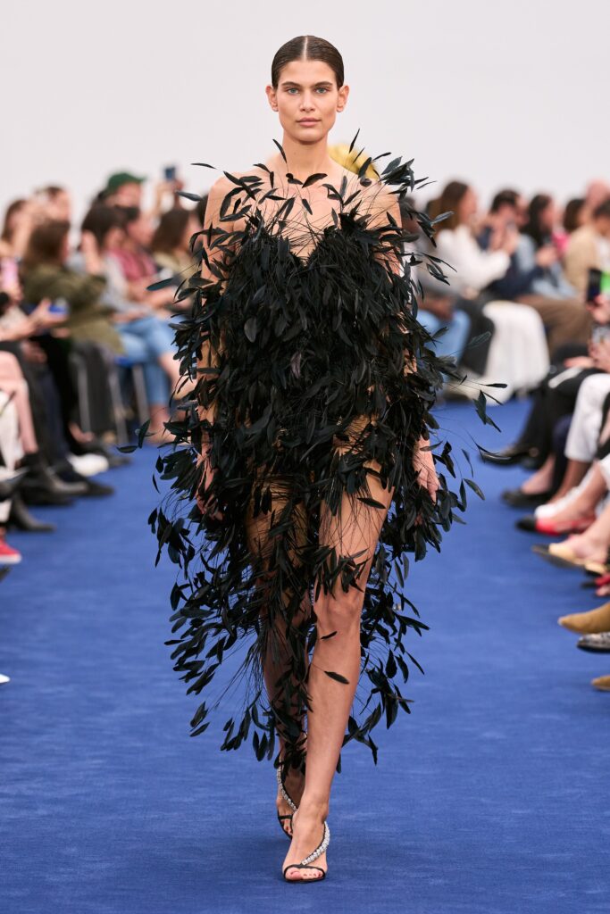 A fitted black feather sleeveless dress with a V-neckline and asymmetric design.