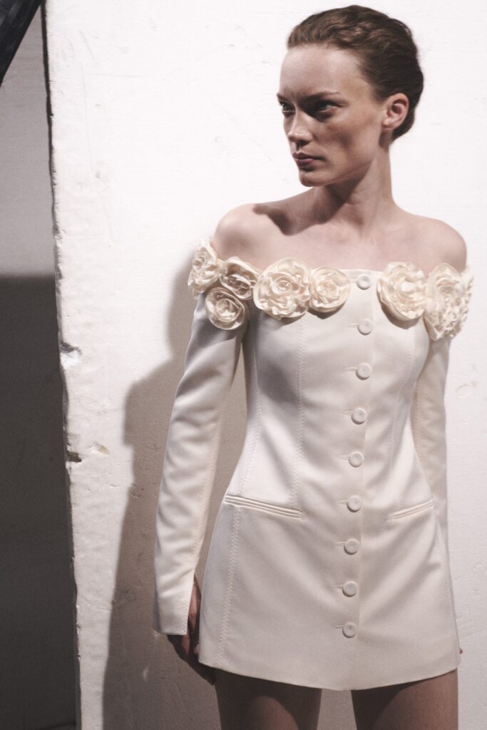 A fitted white silk dress with off-shoulder design and embroidered floral details.