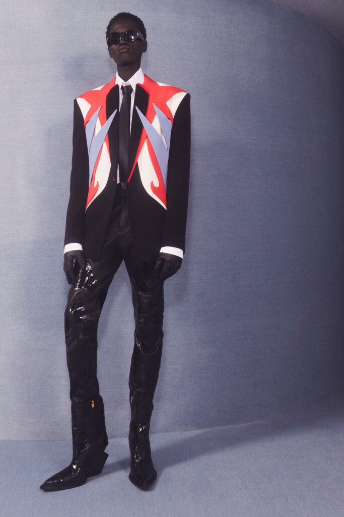 An oversized black leather jacket with red and blue accents paired with fitted black pants.